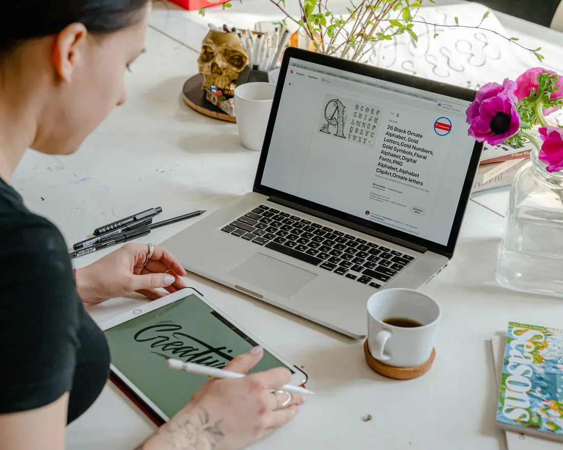 Graphic designer hand-lettering a logo on a tablet beside a laptop