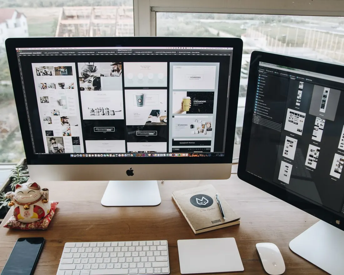 Website page designs laid out on two desktop screens in a design studio